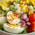 Colorful egg and avocado salad with cherry tomatoes, red onion, corn, and feta cheese, topped with fresh cilantro.