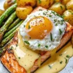 Poached egg on salmon with creamy sauce, roasted potatoes, and grilled asparagus on a plate.