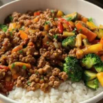 A close-up of a savory ground turkey rice bowl with sautéed mushrooms, roasted zucchini, bell peppers, broccoli, and white rice in a white bowl.