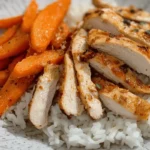 A bowl of spicy grilled chicken over white rice, topped with roasted carrots, fresh herbs, and a creamy sauce.