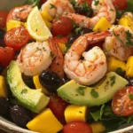 A vibrant tropical shrimp salad with avocado, mango, cherry tomatoes, olives, and lemon wedges.